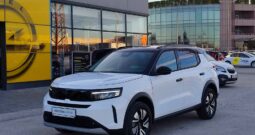 White Opel Frontera Hybrid SUV parked outside a modern car showroom with large glass windows behind it.