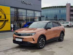 Orange Opel Grandland Hybrid SUV parked outside a modern dealership with glass storefront and a Cyrillic sign above the entrance, reflecting in the windows.