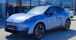 Blue compact electric SUV in a dealership lot, shown from the front-left side with a glass showroom in the background.